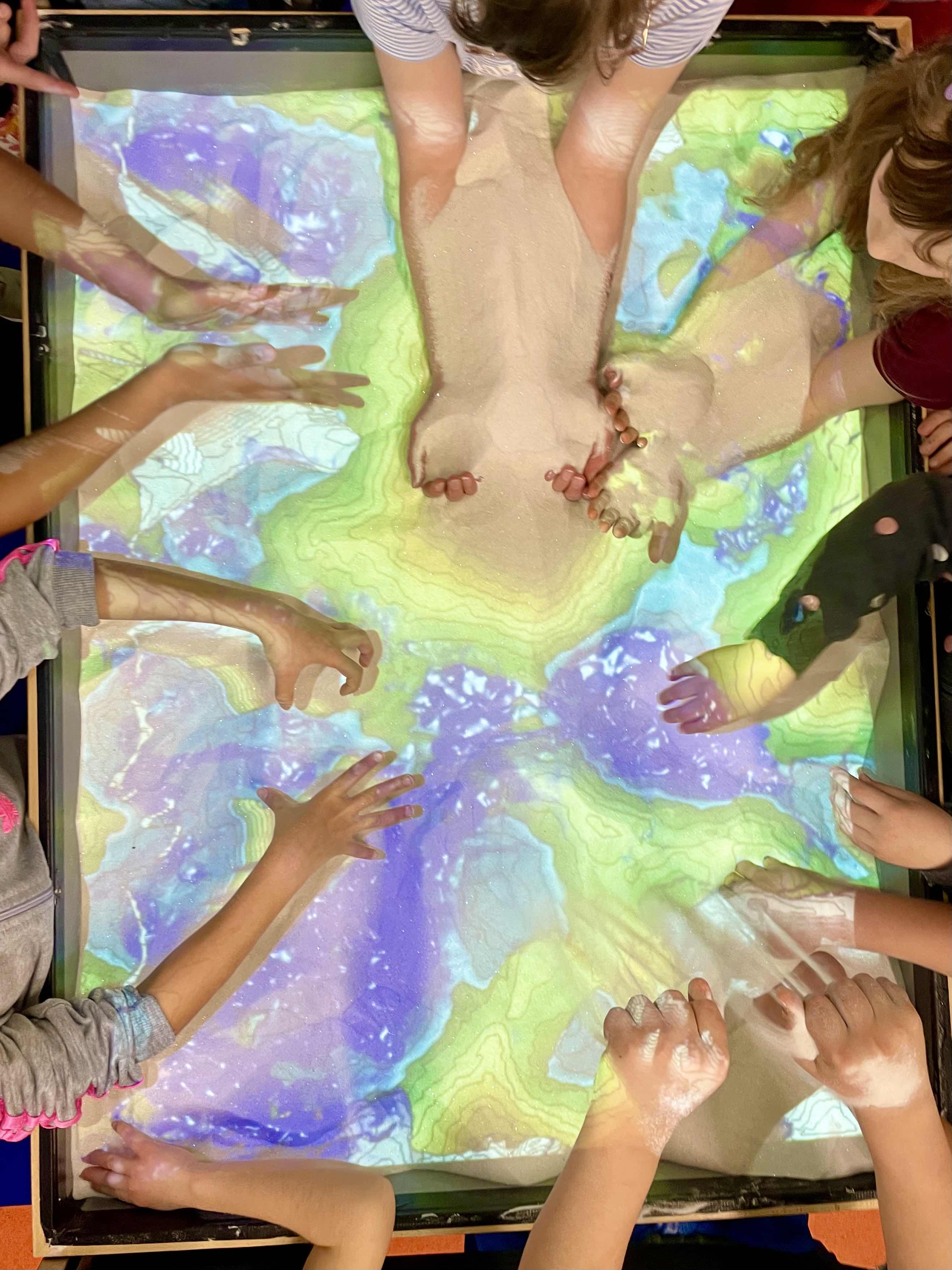 a photo of hands of children at the augmented reality sandbox