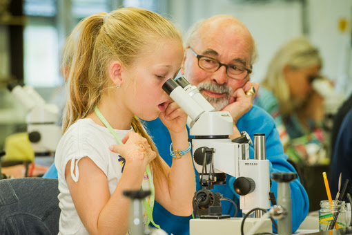 Ein Mädchen beim Mikroskop und ein alter Mann daneben